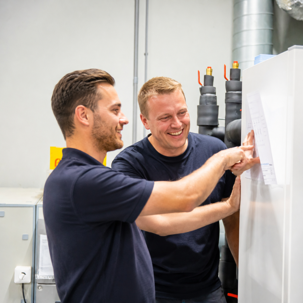 Twee lachende monteurs bekijken een installatie in een technische ruimte