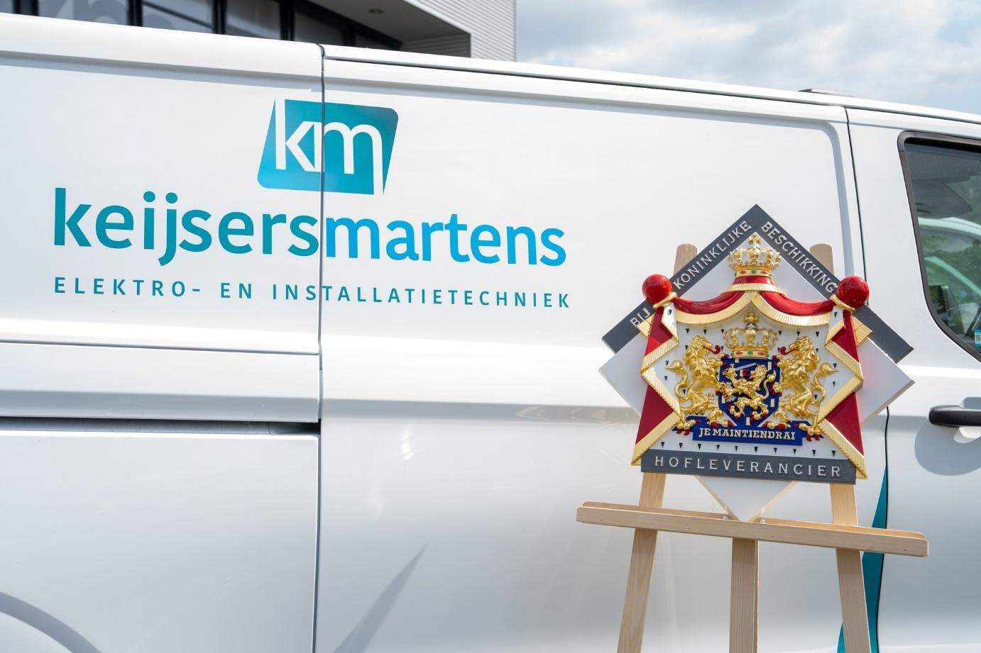 Wapenbord van het predicaat Hofleverancier naast een bedrijfsbus van Keijsers Martens
