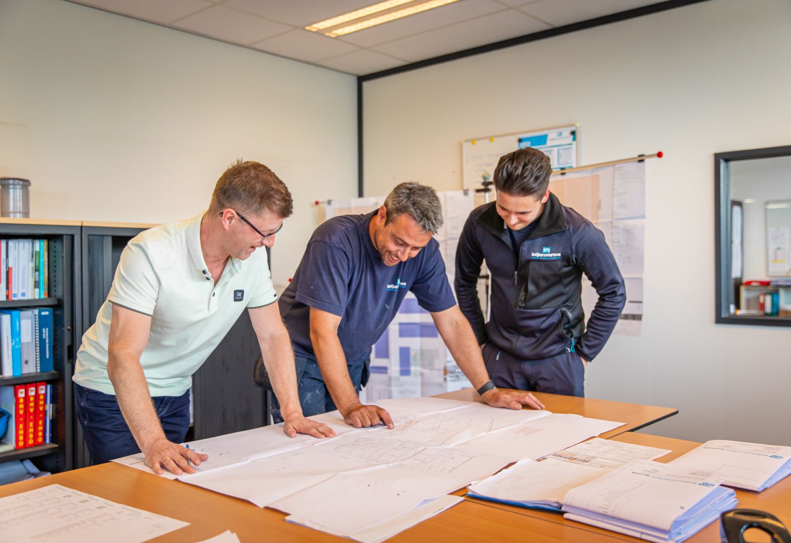 Drie medewerkers bekijken samen bouwtekeningen aan tafel