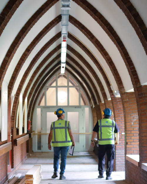 Twee monteurs in veiligheidshesjes lopen door de gang van een historisch gebouw