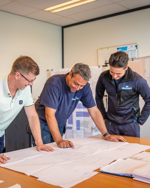 Drie medewerkers bekijken samen bouwtekeningen aan tafel